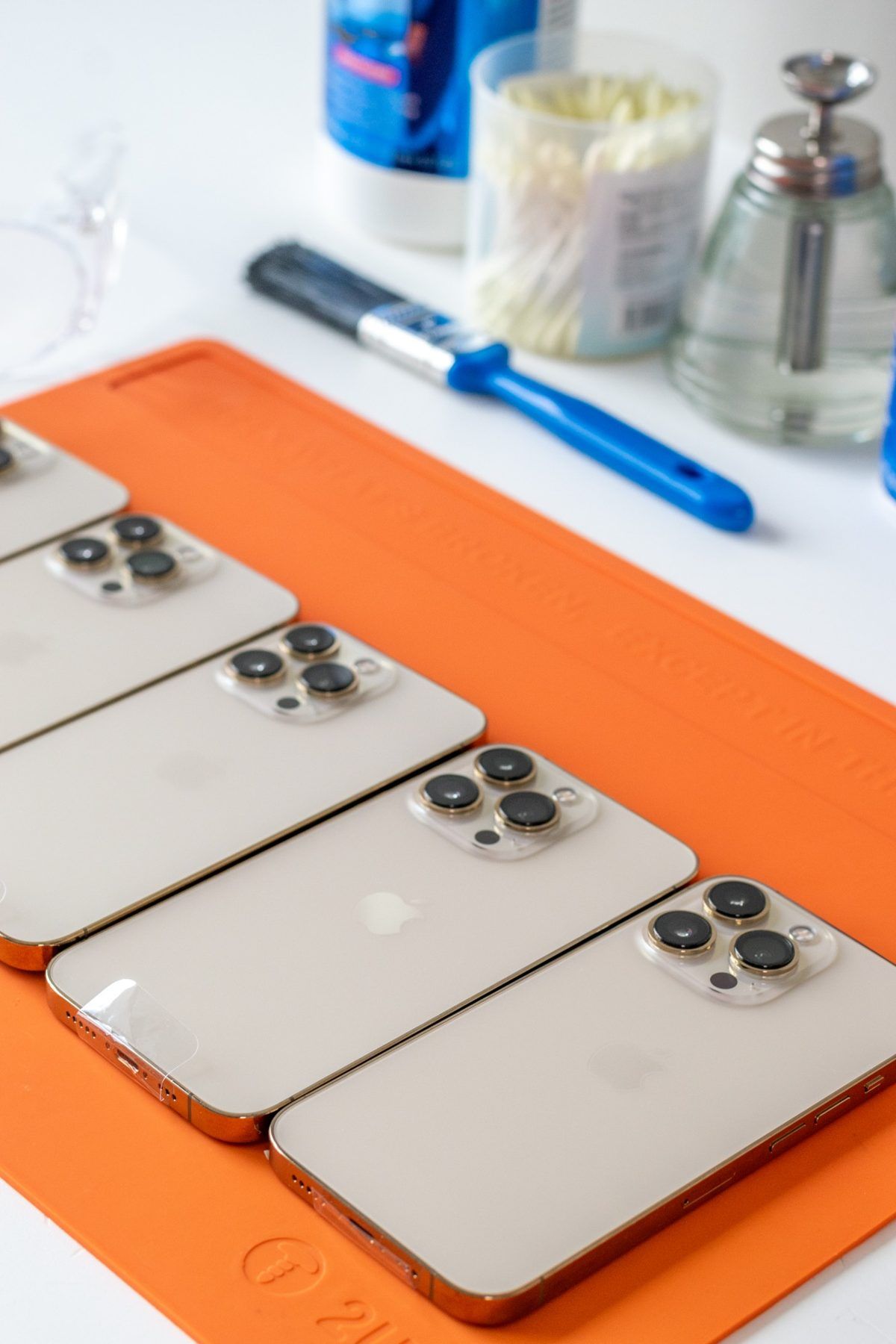 Fila de iPhone Pro sobre un tapete de trabajo naranja, con pincel e hisopos